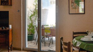 A dining area with a table set for two, a potted plant, and a sliding glass door leading to an outdoor patio.