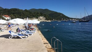 A coastal area with a pier, lounge chairs, and boats.