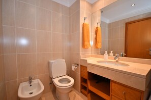 Een badkamer met toilet, bidet, wastafel en spiegel.