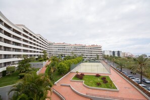 Een meerlaags hotel met een binnentuin, inclusief een tennisbaan, palmbomen en een aangelegde tuin.