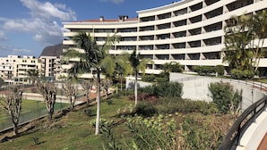 Un hotel de varios pisos con balcones, piscina y zonas verdes circundantes.