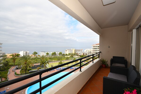 Un balcón con piscina, mobiliario de exterior y vistas al océano y edificios.
