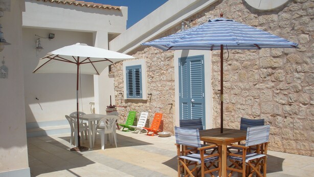An outdoor patio with a table and chairs, a stone wall, and a blue door. - La Meridiana holiday home (Donnalucata ( Ragusa))
