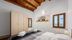 Un dormitorio con cama, armario, un cuadro y ventana con vista al mar.