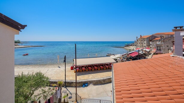 Un pueblo costero con playa, edificios de techo rojo y cielo azul despejado.
