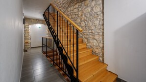 Una escalera de madera con barandales negros que conduce a una habitación con pared de piedra.
