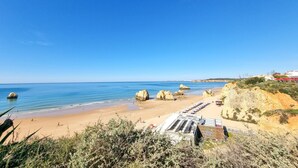 A beach with clear blue water, rocky formations, and a row of beach umbrellas. - Apartment Rocha | Sea View | Concorde Sky (Portimão)