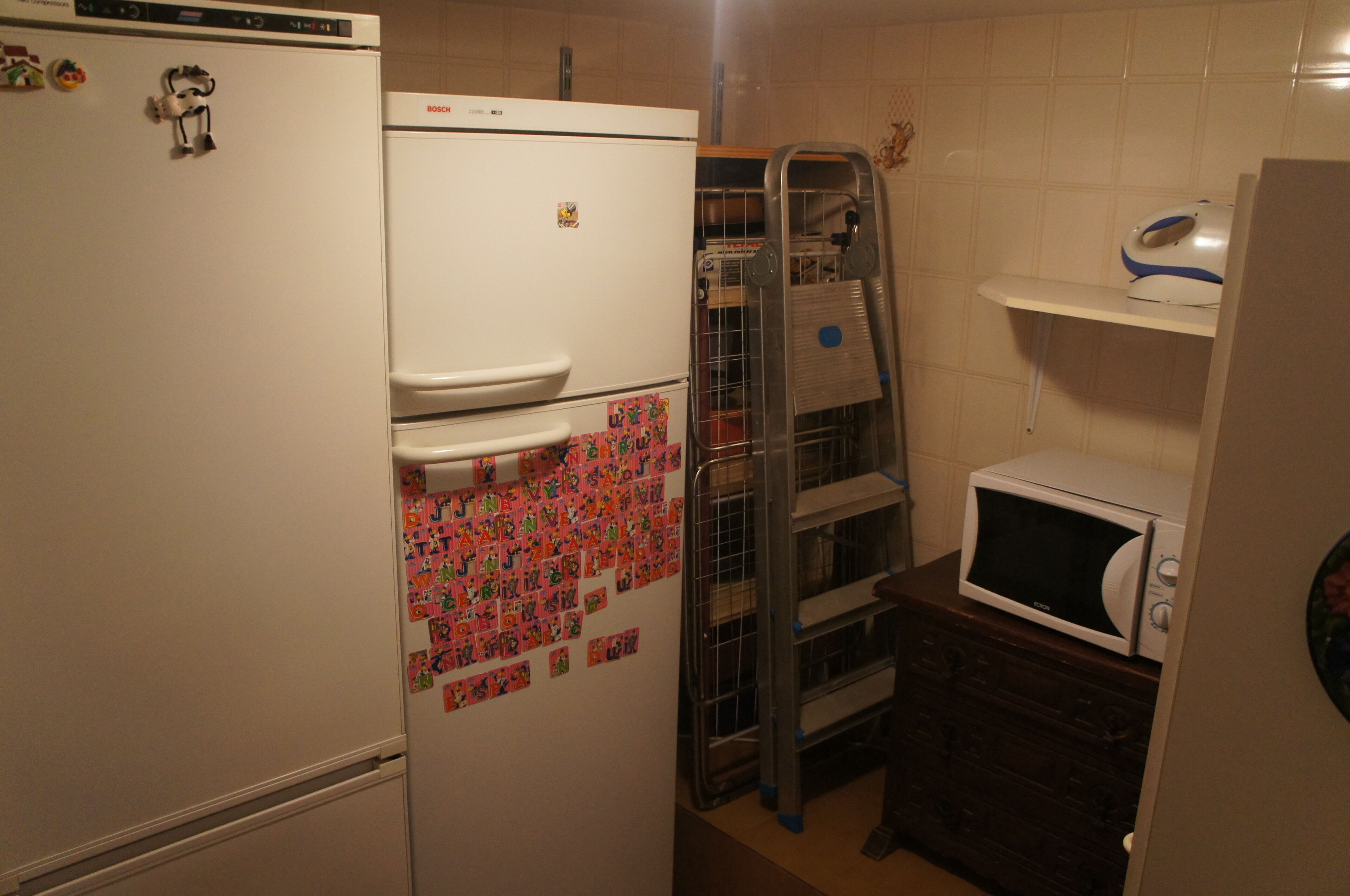 A compact kitchen with a refrigerator, microwave, and a metal drying rack.