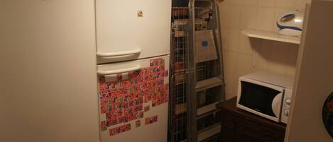 A compact kitchen with a refrigerator, microwave, and a metal drying rack.