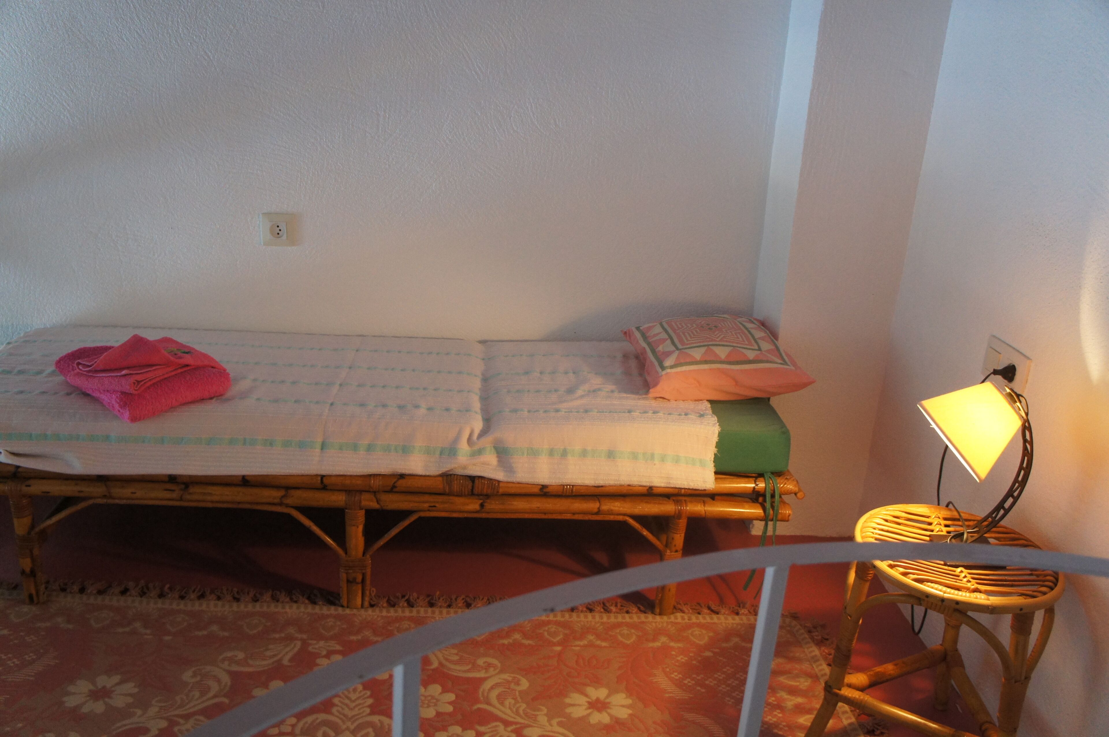 A single bed with a folded blanket and a pillow, a bedside lamp, and a chair.