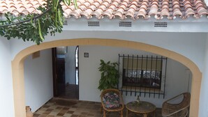An outdoor patio area with a tiled floor, a round table, two wicker chairs, a potted plant, and a window with metal bars. - Minot house with sea and mountain views  (Dénia)