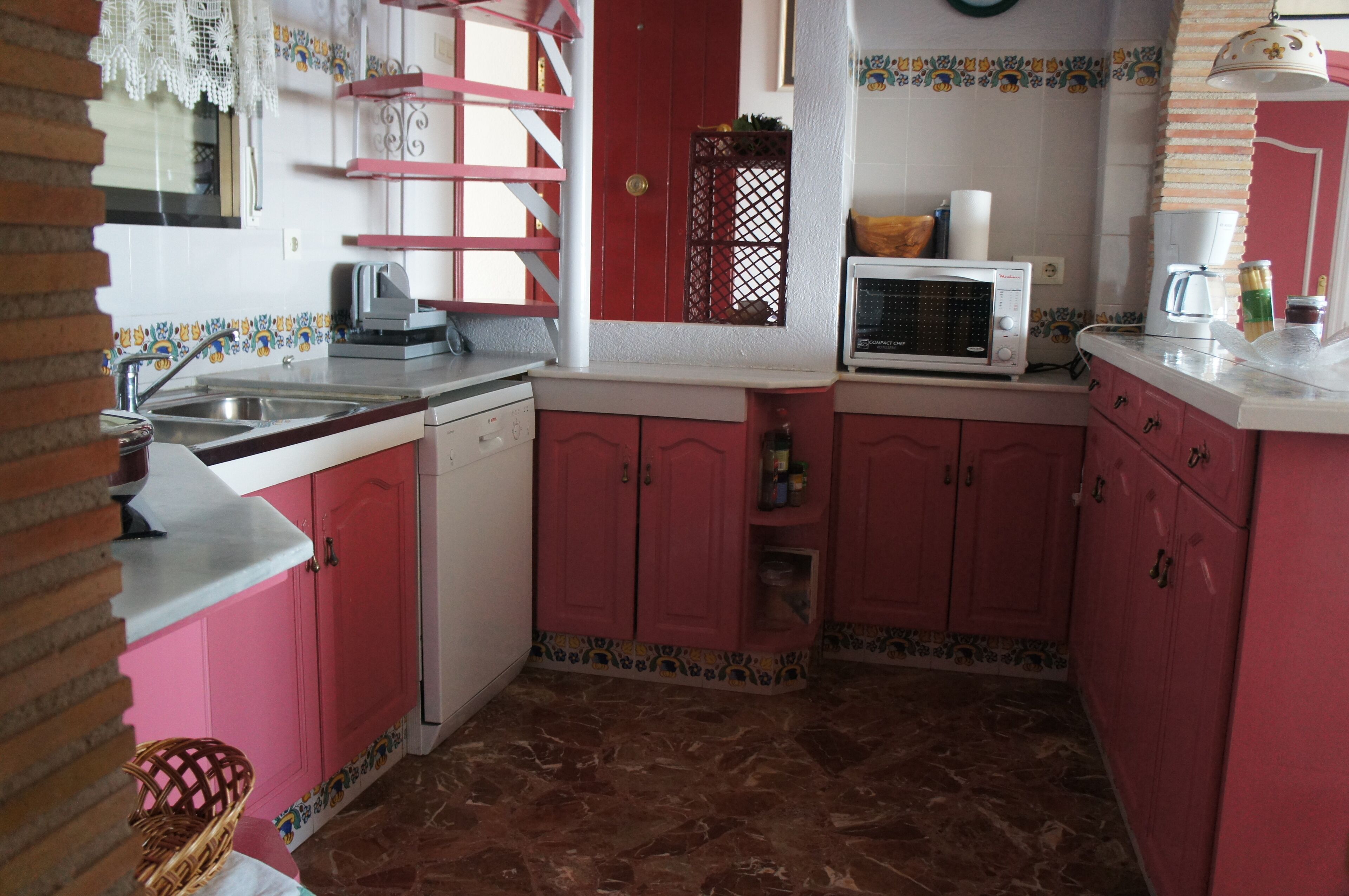 A kitchen with pink cabinets, a microwave, a coffee maker, and a sink.