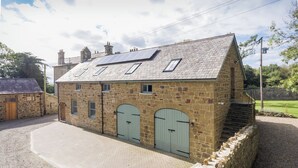 A stone building with a sloped roof, two arched doors, and a paved driveway. - Beautifuly restored Coach House & Granary set in the grounds of Glaneirw Mansion (Cardigan)