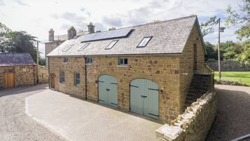 A stone building with a sloped roof, two arched doors, and a paved driveway.
