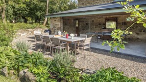 A stone house with a patio area featuring a table and chairs, surrounded by greenery. - Beautifuly restored Coach House & Granary set in the grounds of Glaneirw Mansion (Cardigan)
