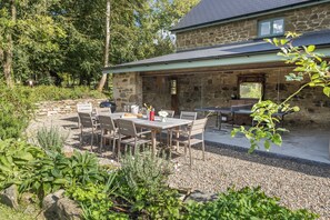 A stone house with a patio area featuring a table and chairs, surrounded by greenery.