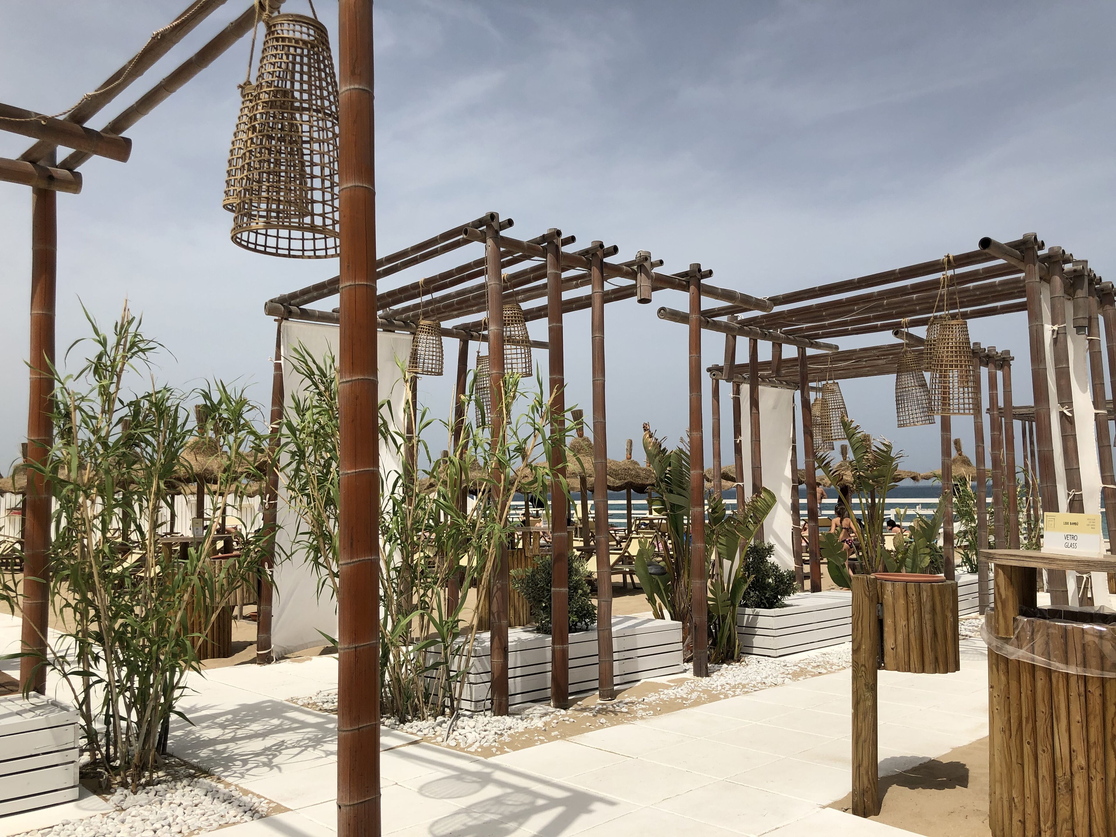 Eine Pergola aus Bambus mit hängenden Lichtern, umgeben von tropischen Pflanzen und einem weiß gefliesten Boden.
