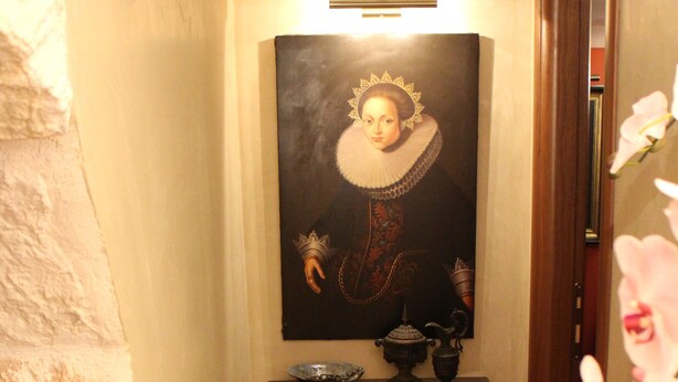 A hallway with a framed portrait, a small table with a bowl and a vase, and a wooden chest.