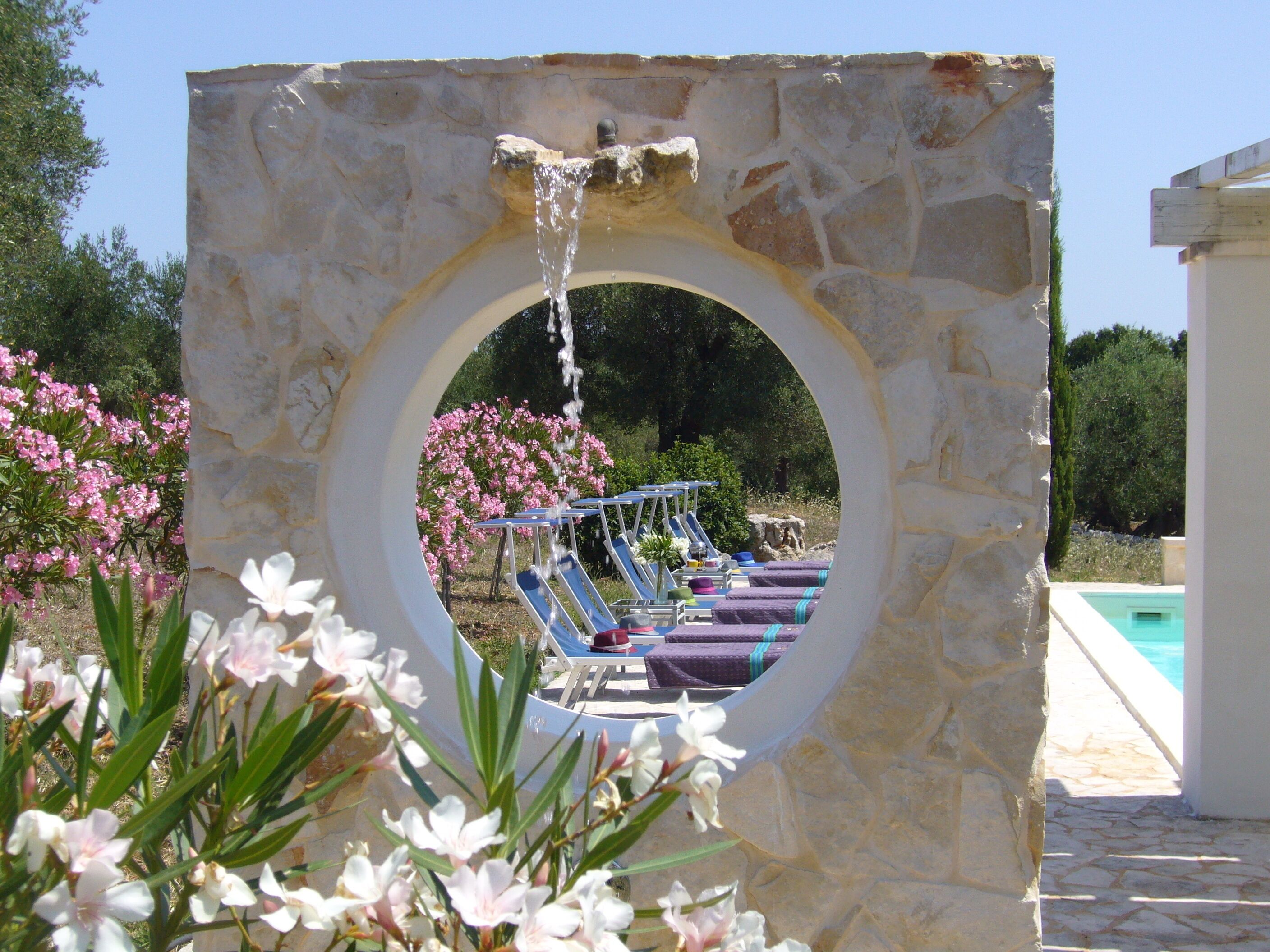 Una construcció de pedra amb una obertura circular, una font d'aigua i una zona de piscina amb gandules.