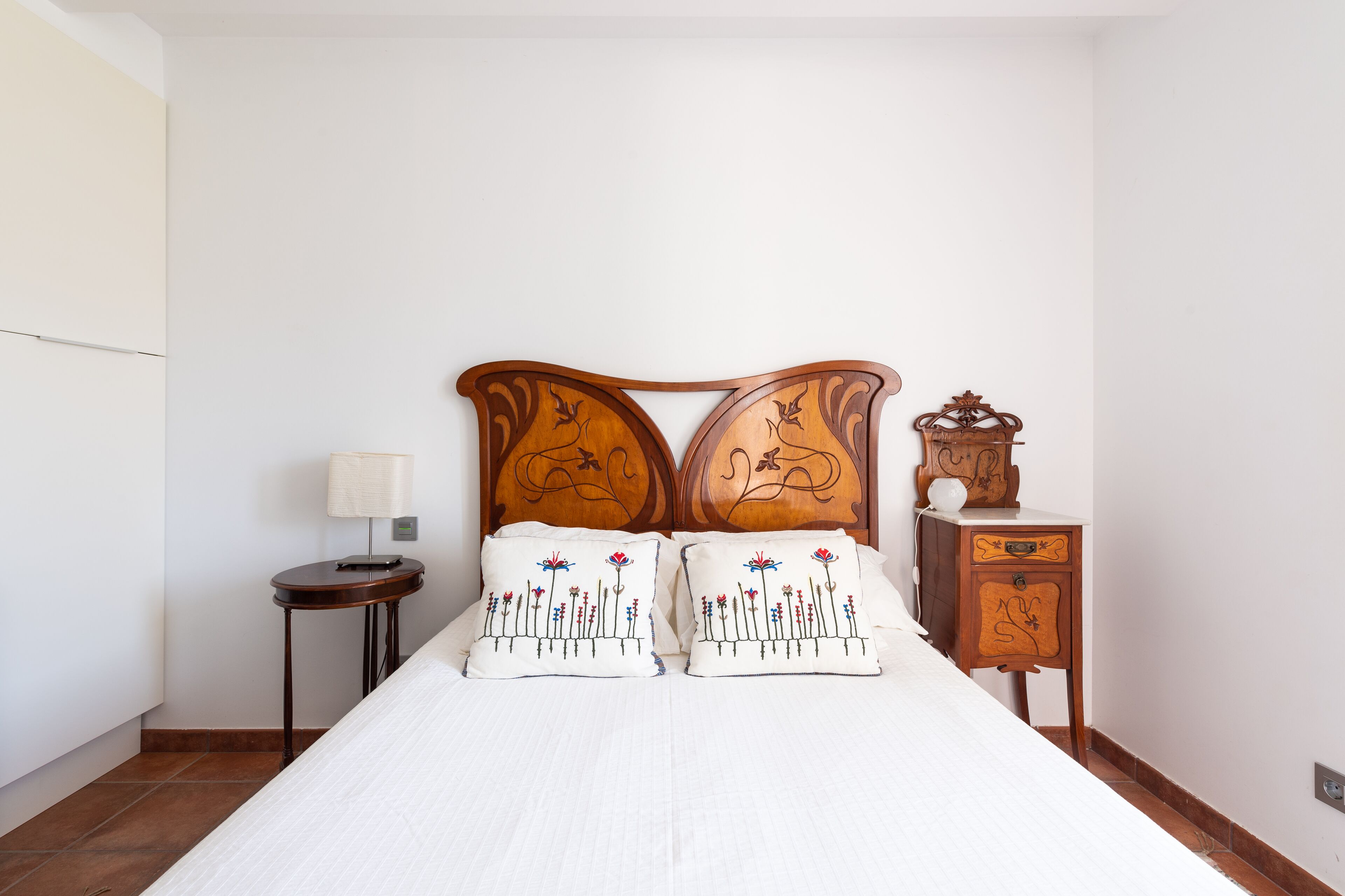 Une chambre à coucher avec une tête de lit en bois, deux tables de chevet, une lampe et une petite table de nuit agrémentée d’un objet décoratif.