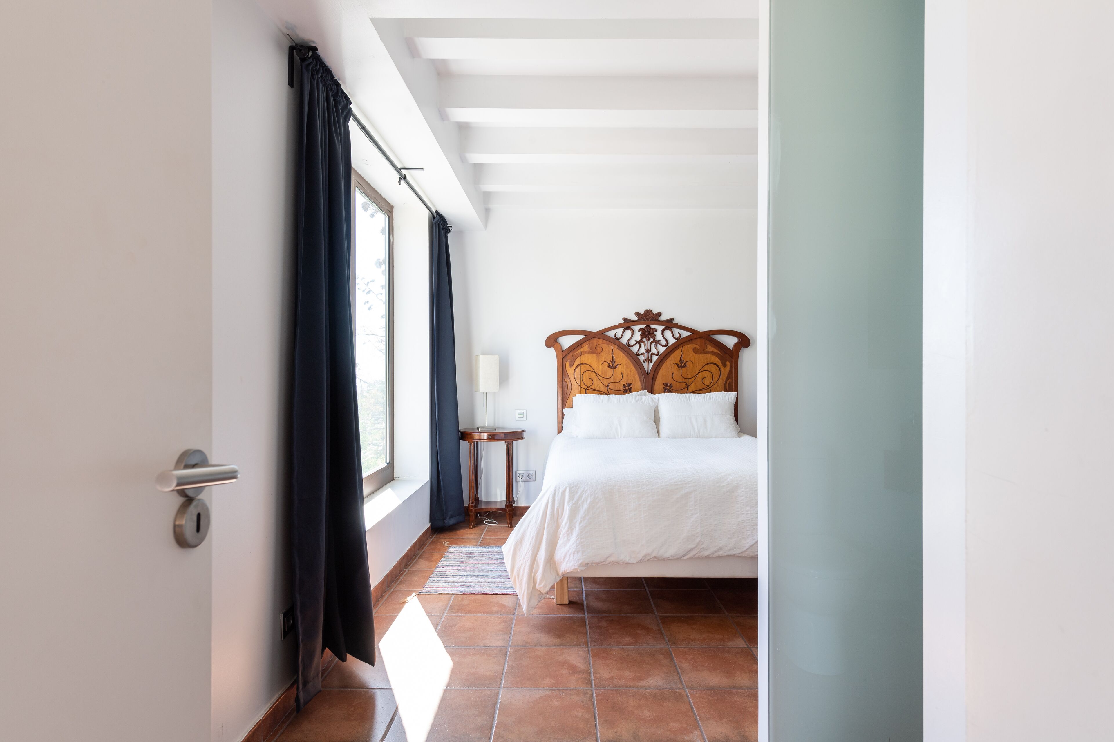 Une chambre à coucher avec un lit, une table de chevet, une lampe et une fenêtre avec des rideaux.