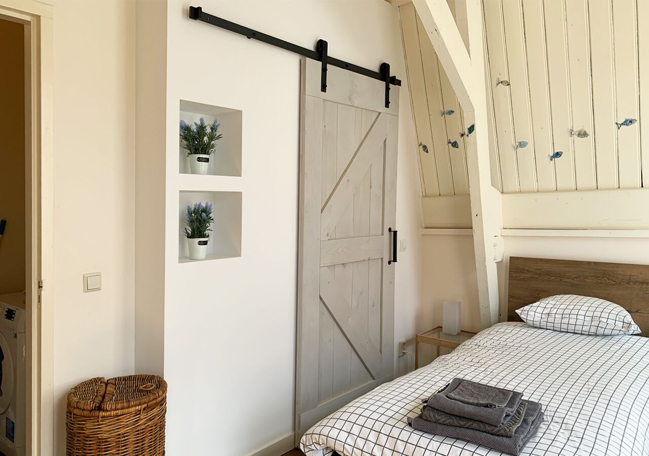 A bedroom with a bed, a sliding barn door, a small shelf with plants, and a wicker basket.