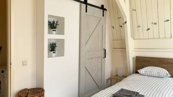 A bedroom with a bed, a sliding barn door, a small shelf with plants, and a wicker basket.