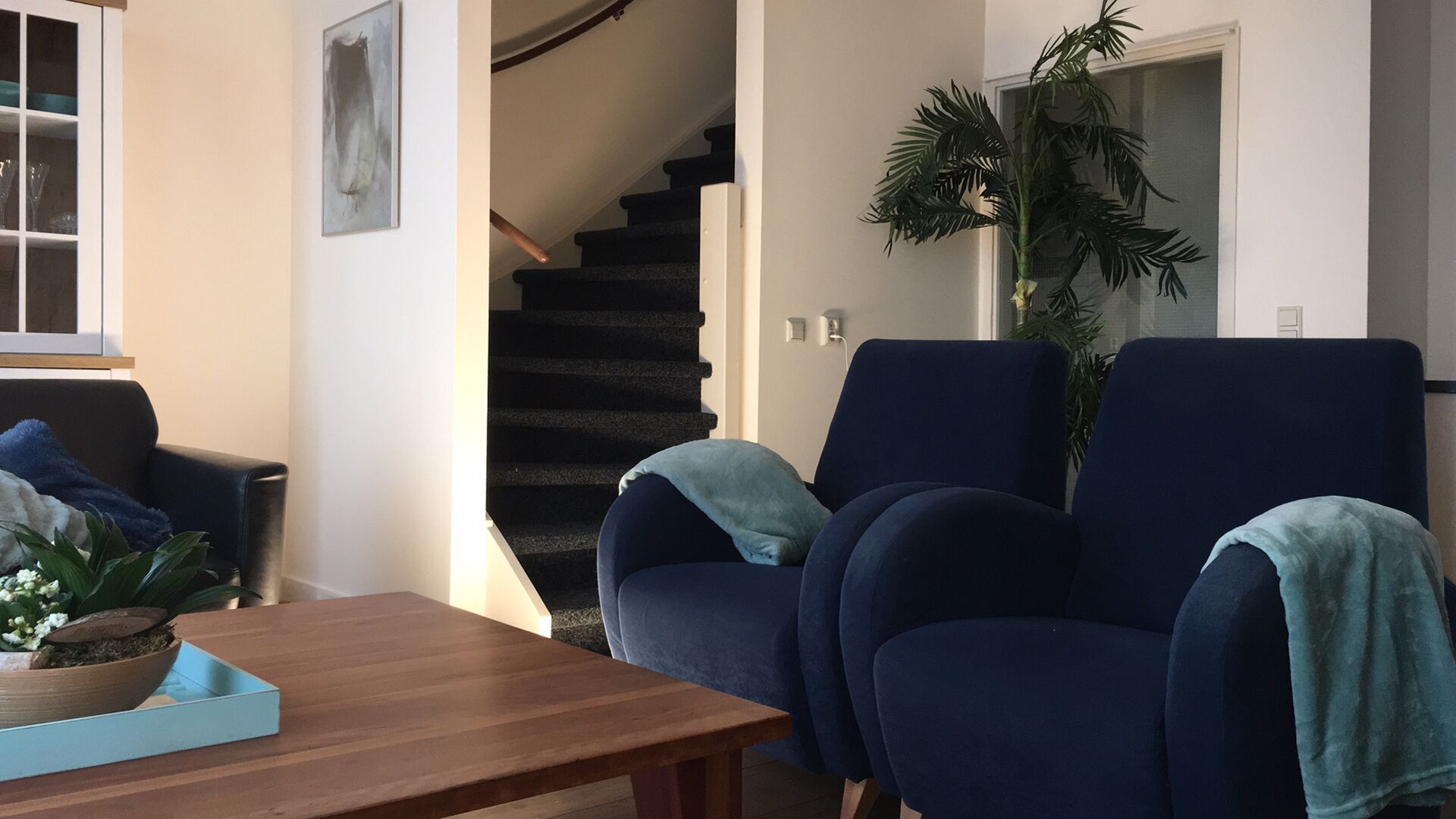 A living room with a dark blue armchair, a wooden coffee table, and a staircase leading to another level.