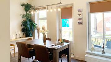 A dining area with a wooden table, brown chairs, a potted plant, and a window with a view of a building.