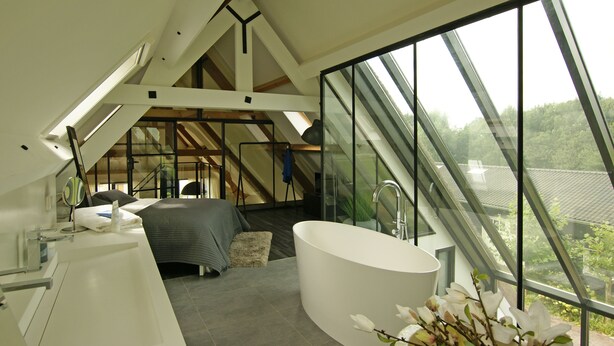 A modern bedroom with a skylight, a large bathtub, and a view of the outdoors.