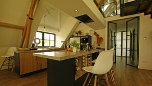A modern kitchen with a central island, wooden beams, and a view to the upper level.