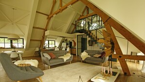 A spacious loft with high ceilings, exposed wooden beams, a central staircase, and a cozy seating area with a fireplace.