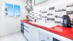 Una cocina moderna con encimera roja, lavavajillas integrado y un amplio ventanal con vista a la ciudad.