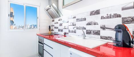 A modern kitchen with a red countertop, a built-in dishwasher, and a large window with a city view.