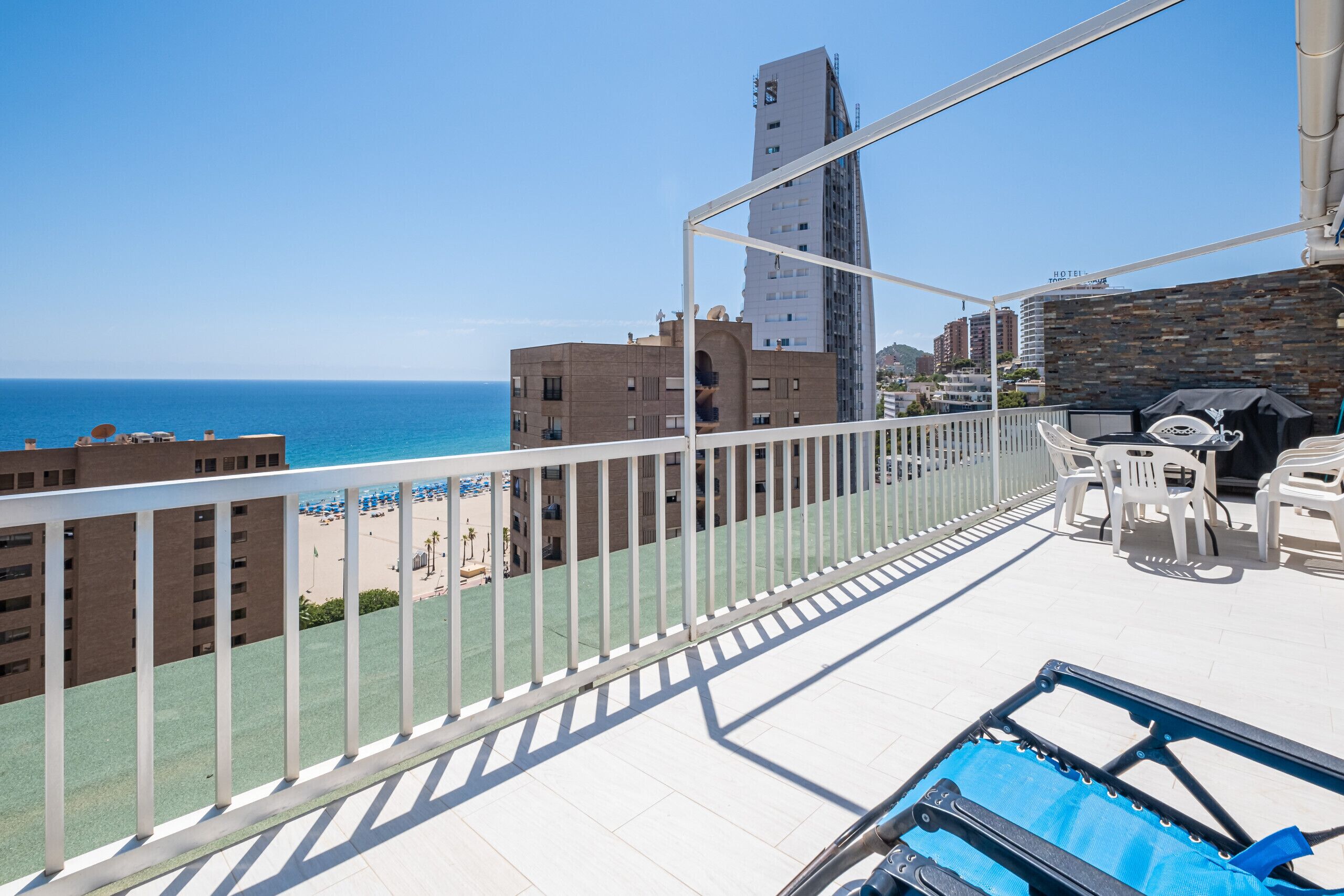 Ein Balkon mit Blick auf Strand und Meer, ein Poolbereich mit Liegestühlen und eine Steinmauer.