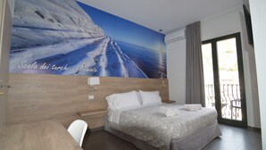 Un dormitorio con un mural grande de un paisaje nevado, una cama con sábanas blancas, una mesita de noche de madera y vistas al exterior a través de una puerta corrediza.