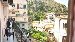 Un balcón con mobiliario exterior, vista a una colina y edificios con balcones y ventanas.