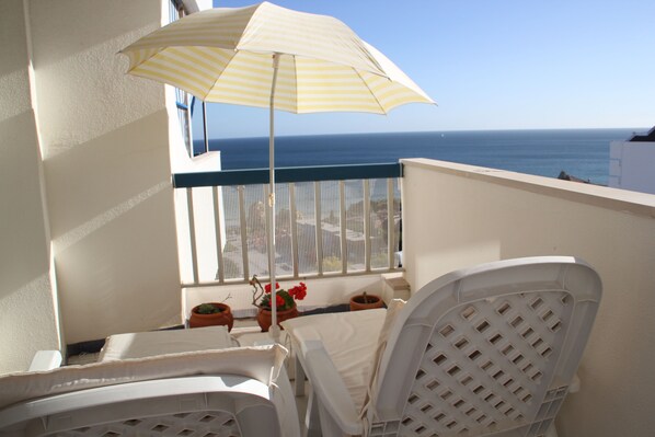 A balcony with a view of the sea, white chairs, a striped umbrella, and potted plants. - Dream Vacation in Praia da Rocha - T1 Sea View (Portimão)