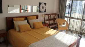 Um quarto com uma cama grande, uma cadeira, uma mesa de cabeceira, uma luminária e uma janela com cortinas.