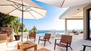 An outdoor patio with wooden furniture, a large umbrella, and a view of the sea. - VILLA HILLTOP (Nuestra Sra de Jesus)