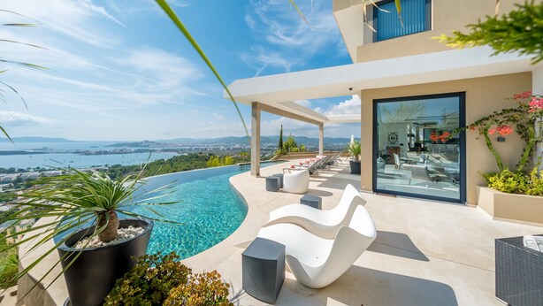 A modern outdoor pool area with a curved edge, lounge chairs, and a view of the sea. - VILLA HILLTOP (Nuestra Sra de Jesus)