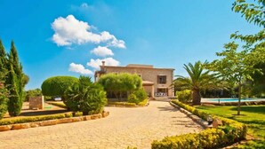 A villa with a paved driveway, a swimming pool, and well-maintained gardens.