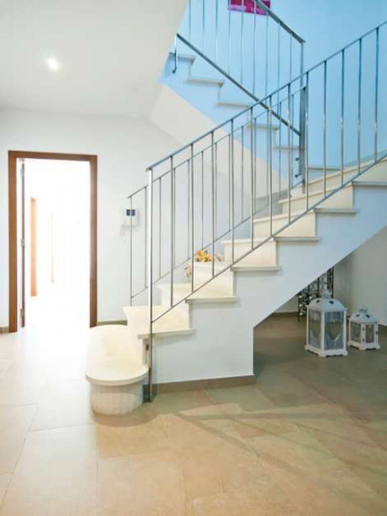 A modern interior with a glass staircase, white walls, and a tiled floor.