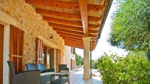 A covered outdoor seating area with stone walls and wooden beams, featuring wicker furniture and a view of greenery.