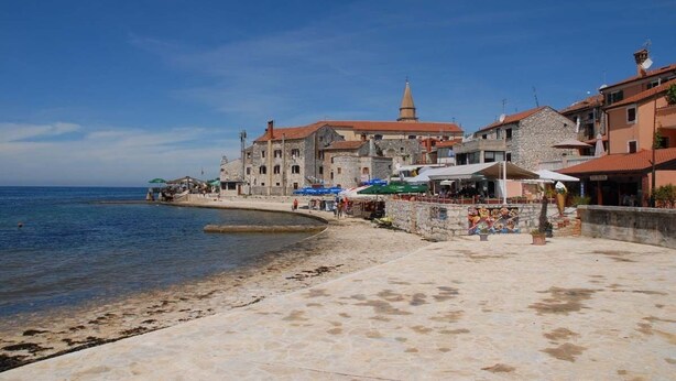 A coastal town with stone buildings, a clear blue sky, and a sandy beach. - Pink apartment with two terraces, garden, a stone's throw from the beach (Umag)
