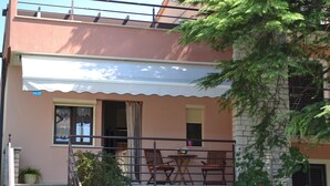 A two-story building with a balcony, a small table, and chairs. - Pink apartment with two terraces, garden, a stone's throw from the beach (Umag)