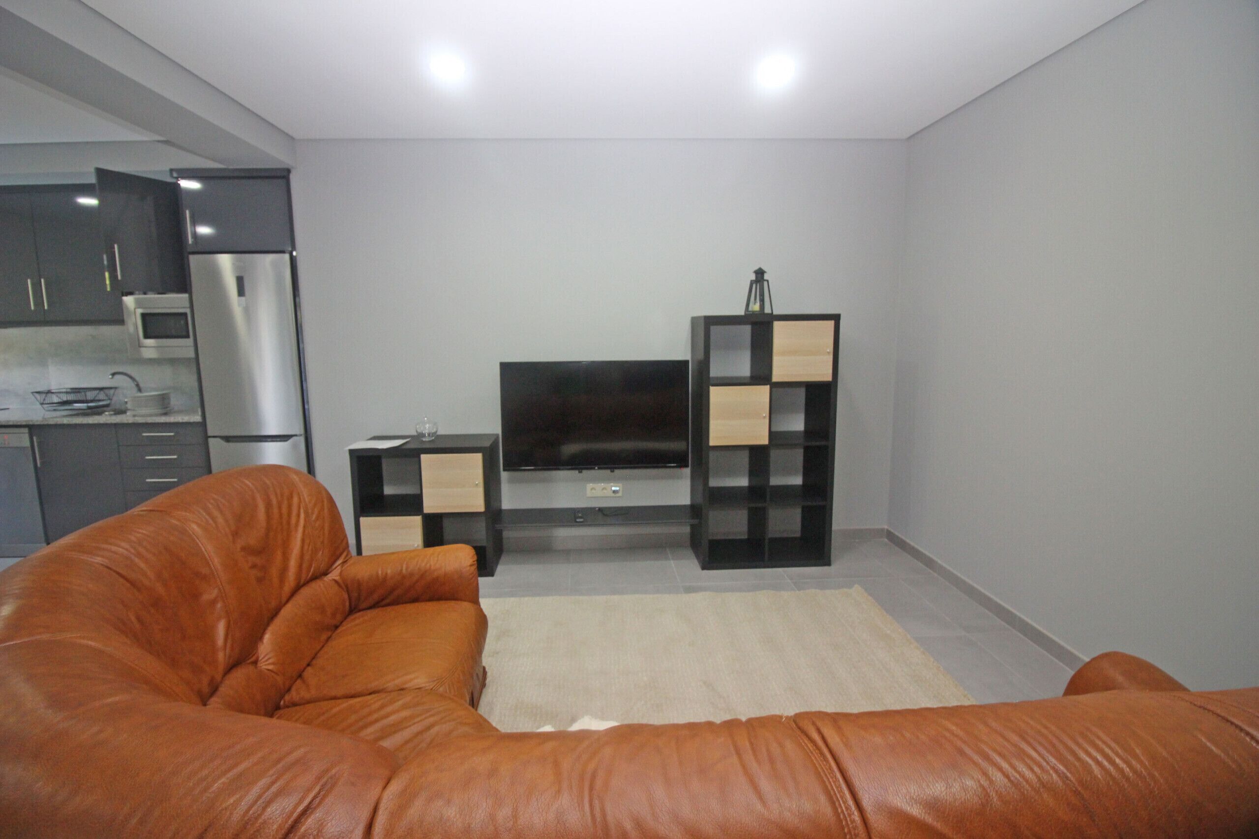 Een moderne woonkamer met een leren bank, een flatscreen televisie en een minimalistische wandplank.