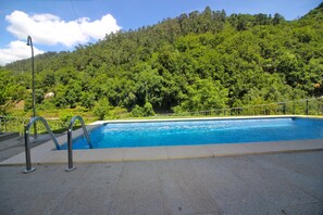 A swimming pool with a metal ladder, surrounded by a concrete deck, set against a backdrop of lush green hills. - House with private pool near Gerês (Terras de Bouro)