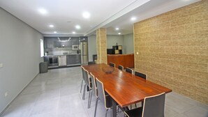 A spacious dining area with a long wooden table and chairs, a kitchen in the background, and a textured wall on one side. - House with private pool near Gerês (Terras de Bouro)