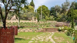 A garden with a stone pathway, wooden benches, and a decorative metal fence.